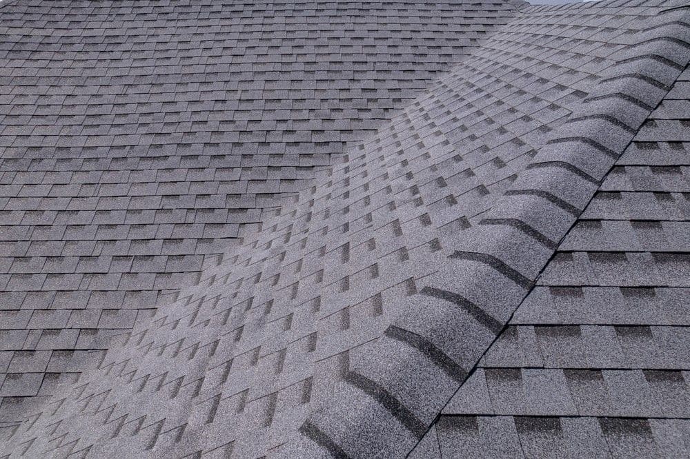 Gray asphalt shingle roof with detailed texture and overlapping pattern. The shingles create a uniform, orderly appearance, conveying durability.