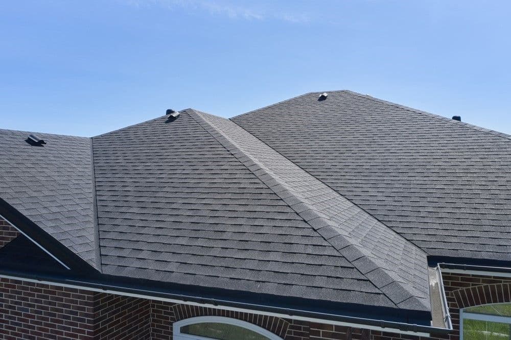 Aerial view of a house with a new, well-installed, gray asphalt shingle roof against a clear blue sky. The roof has clean lines and a modern appearance.