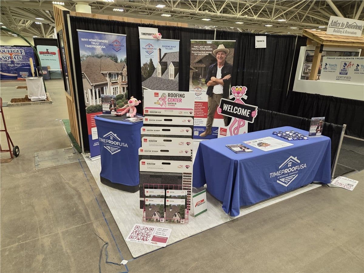 Booth display at a trade show featuring "TimeProofUSA" with blue table covers, roofing samples, brochures, and welcome signage. The scene conveys professionalism and inviting atmosphere.