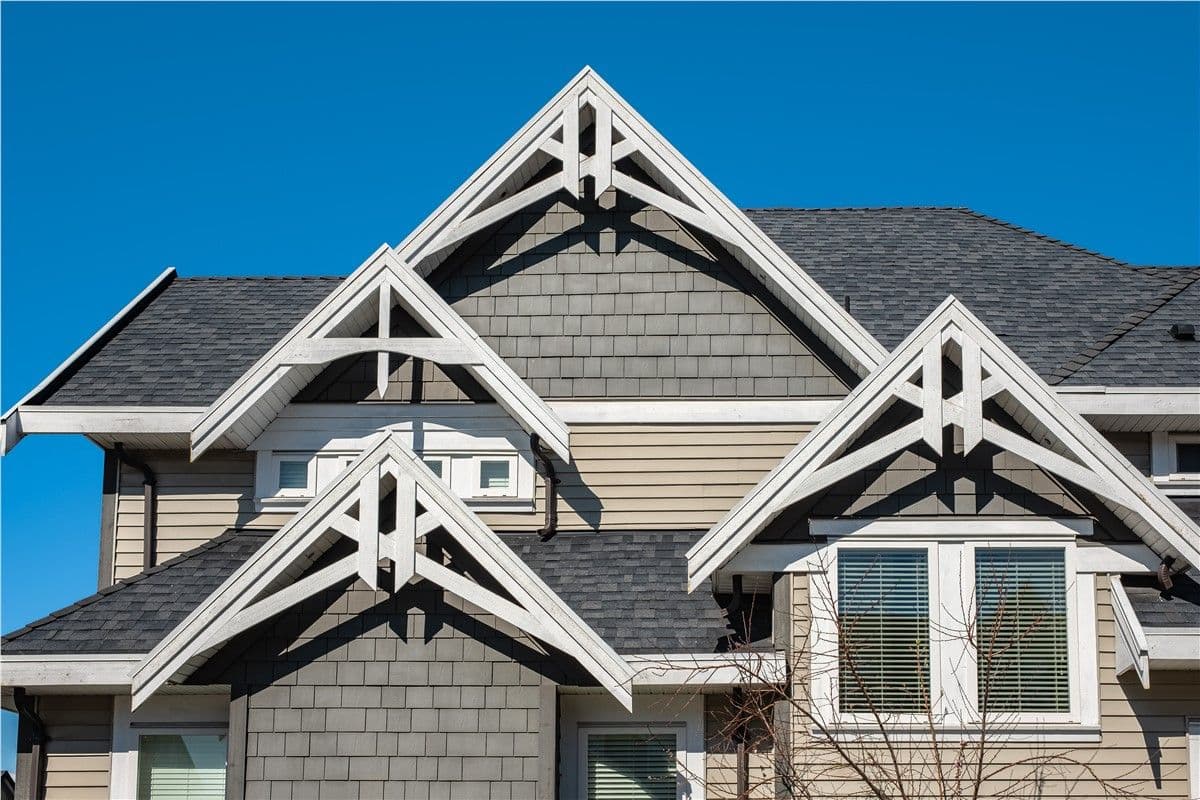 Close-up of a house exterior with gabled roofs, gray siding, and white trim under a clear blue sky, conveying a clean, modern look.