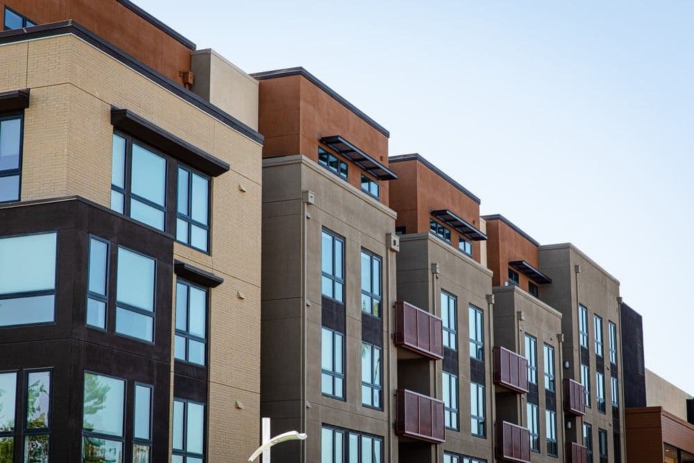 Modern urban apartment building with multiple stories, featuring large windows and balconies. The façade includes neutral tones and clean lines.