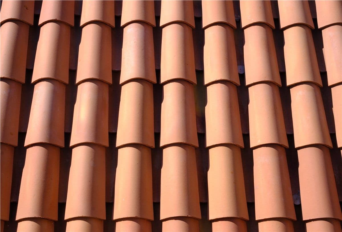 Close-up of a terracotta roof with neatly aligned, curved tiles in natural light. The repetitive pattern creates a warm, orderly texture.
