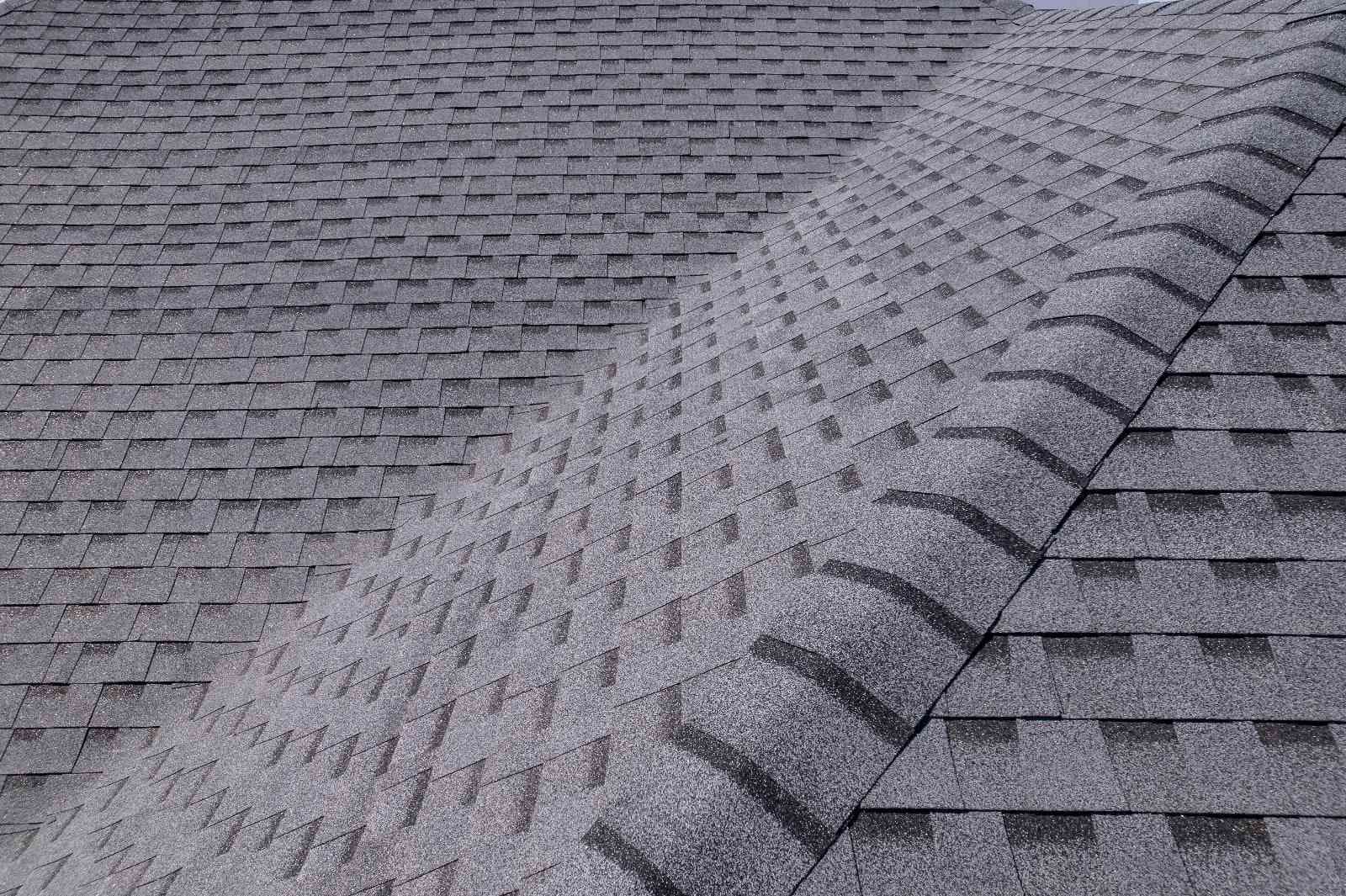 Gray asphalt shingles form a complex roof pattern with a distinct ridge line in the center, creating a textured, geometric appearance.