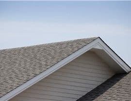 A gable roof with gray shingles and white siding is shown against a clear blue sky. The scene conveys simplicity and tranquility.