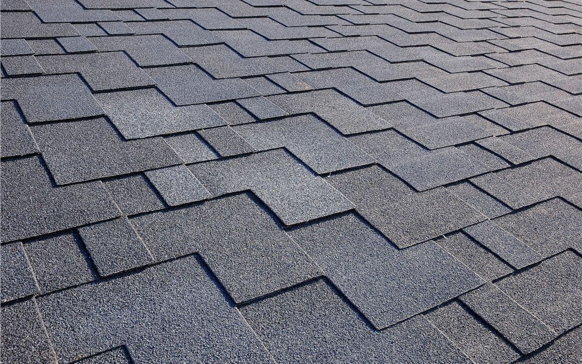 Gray roof shingles in a neat, overlapping pattern, creating a textured grid. The image conveys a sense of order and modern durability.