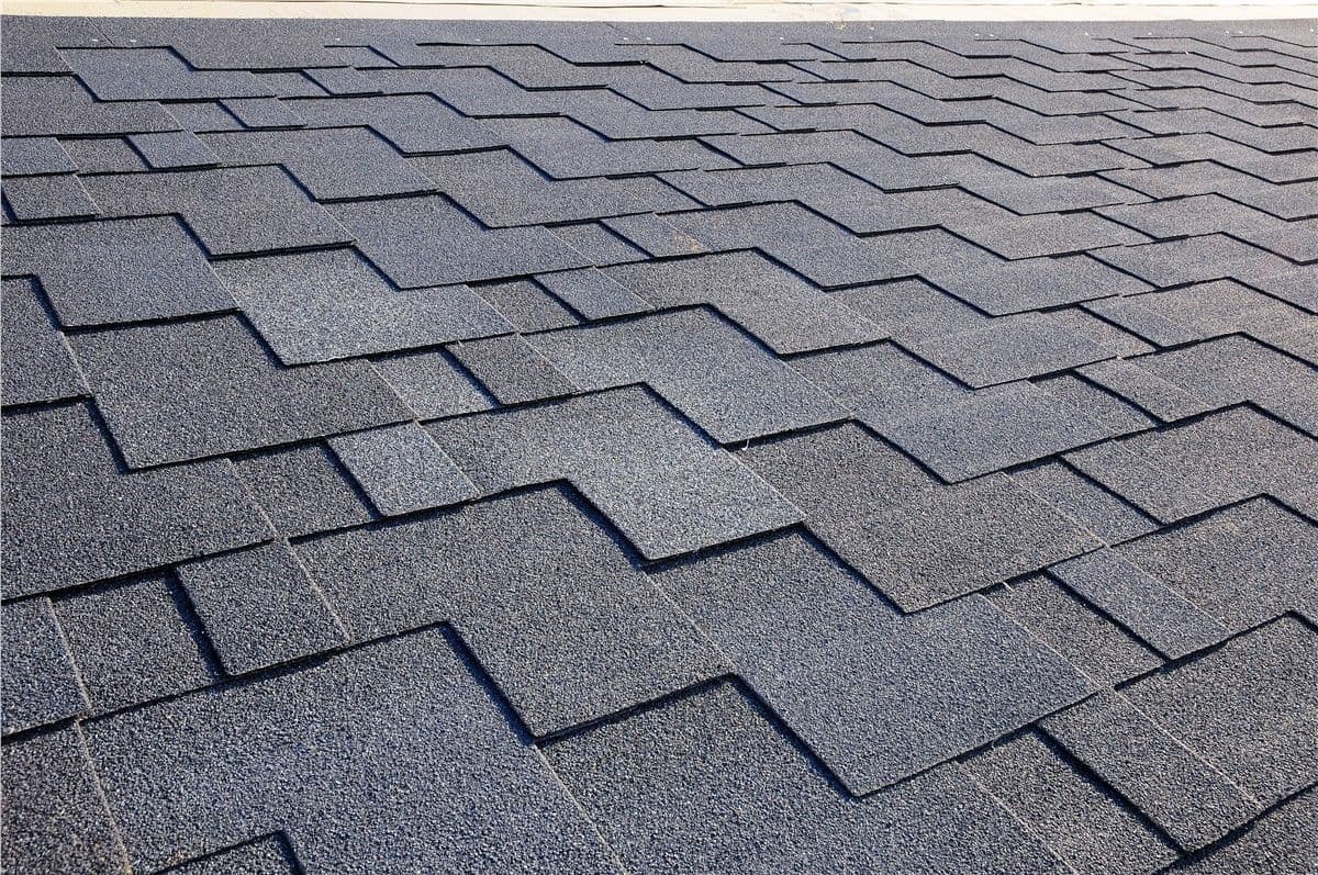 Gray roof shingles in a neat, overlapping pattern, creating a textured grid. The image conveys a sense of order and modern durability.