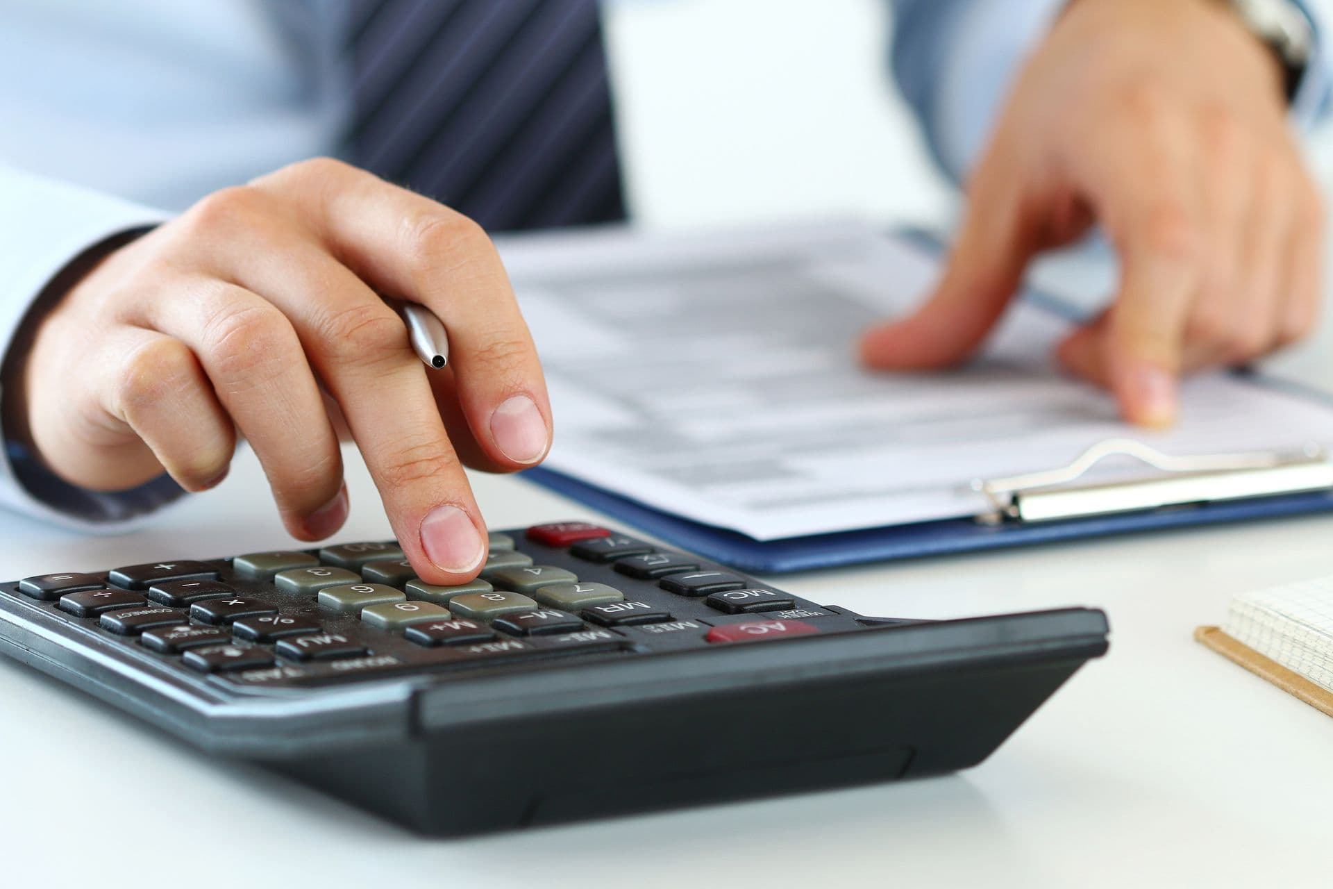 A person in a suit uses a calculator and holds a pen over financial documents. The setting is professional, conveying focus and precision.