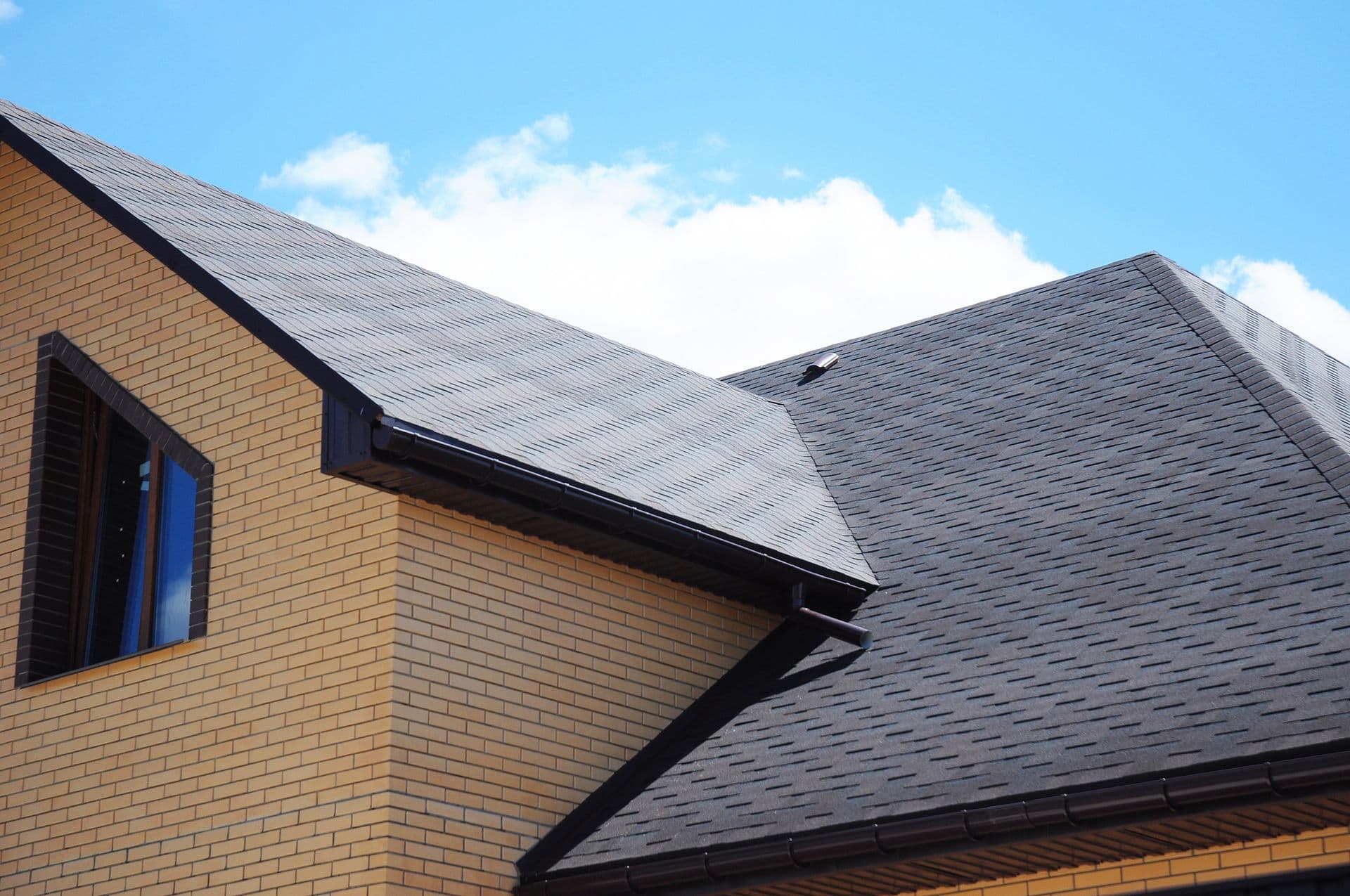 A modern house with a steep, gray shingled roof and yellow brick walls under a clear blue sky, exuding a sense of stability and elegance.