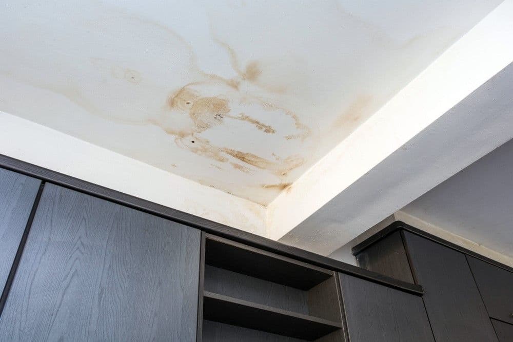 Ceiling with prominent water stains and discoloration above sleek gray cabinets, indicating possible water damage and maintenance issues.