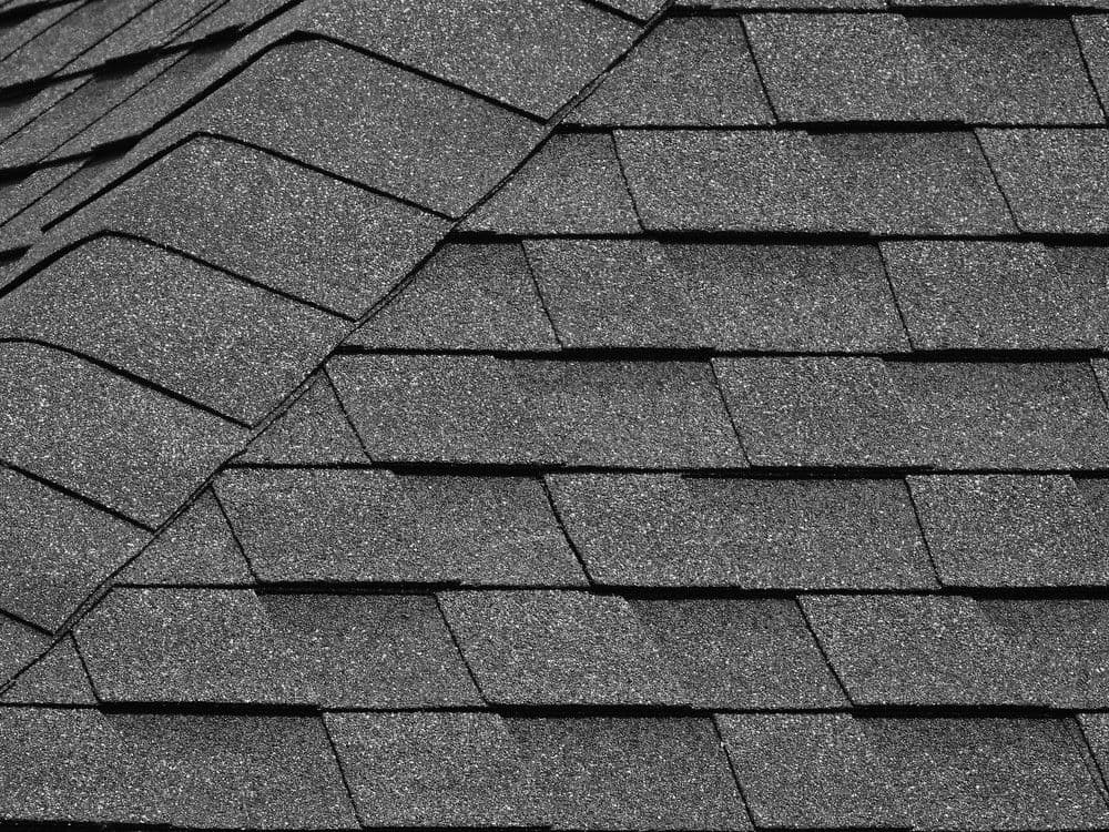 Close-up of a gray asphalt shingle roof, showing overlapping rectangular shingles. The texture is rough, suggesting durability and functionality.