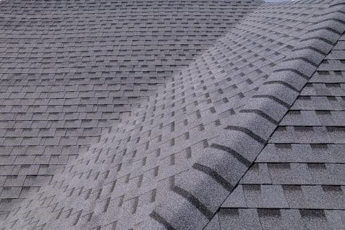 Gray asphalt shingles cover a roof with a prominent ridge running diagonally, creating a geometric pattern. The scene is calm and orderly.