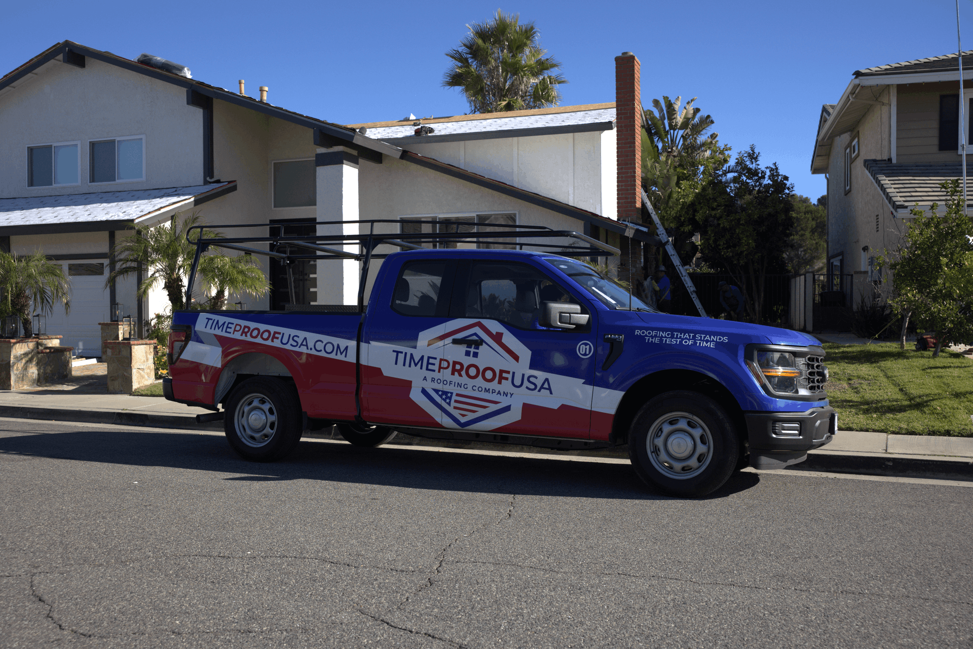 A blue and red truck with "TimeProofUSA" branding and a ladder rack is parked in front of a suburban house on a sunny day.