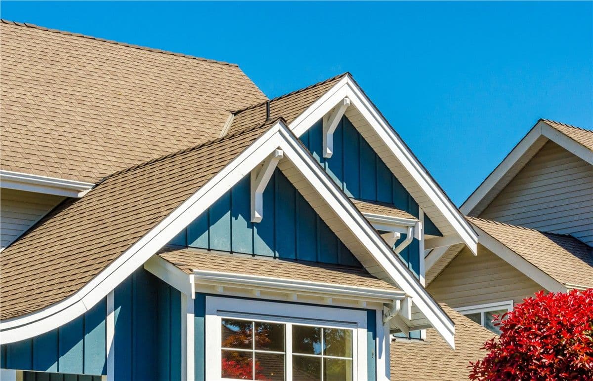 Close-up of a modern house with blue siding and beige roof shingles against a clear sky. Bright red foliage adds contrast, creating a vibrant, homey feel.