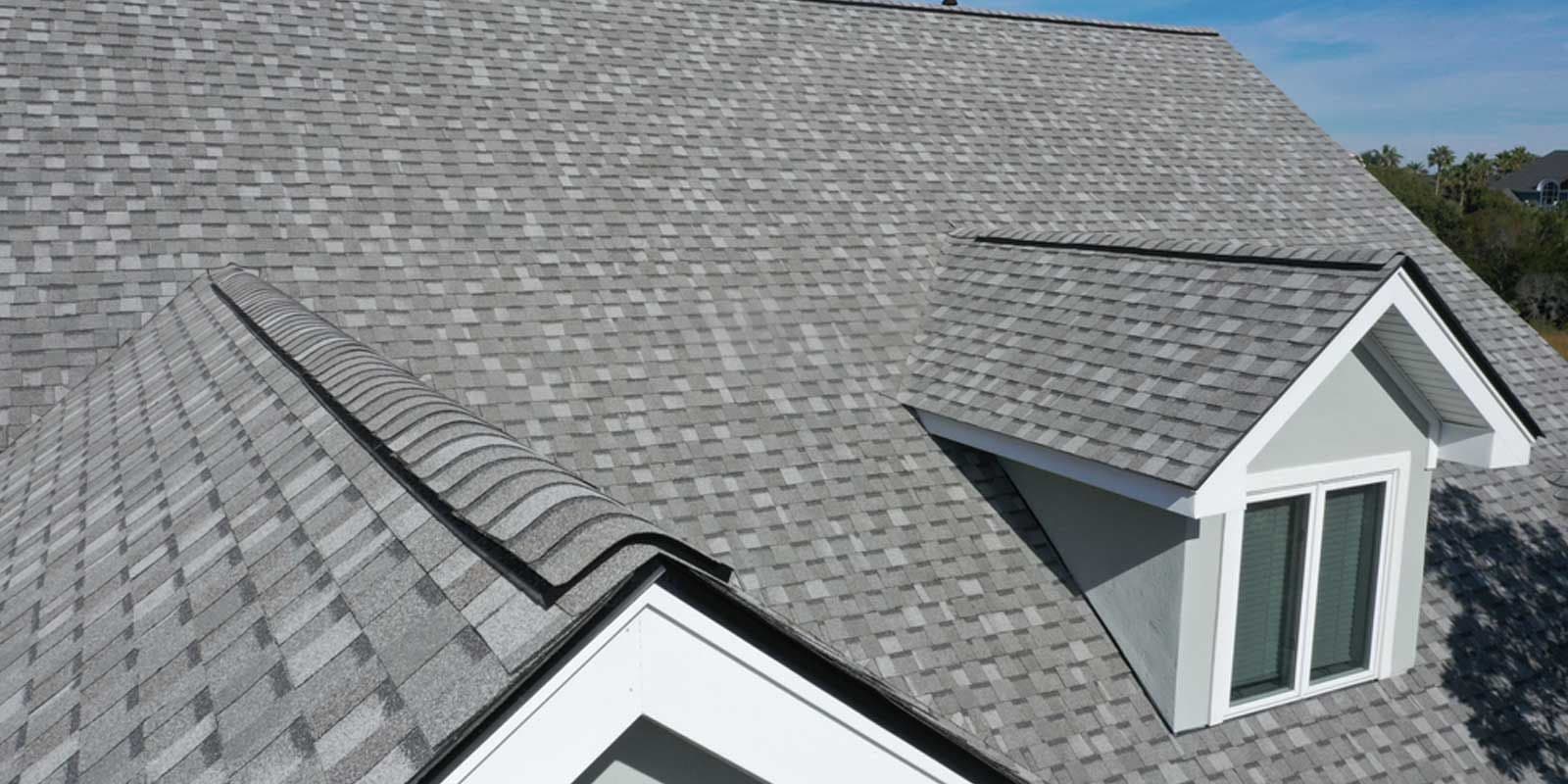 Gray asphalt shingle roof with a dormer window on a sunny day. The shingles are neatly arranged, giving a clean and well-maintained appearance.